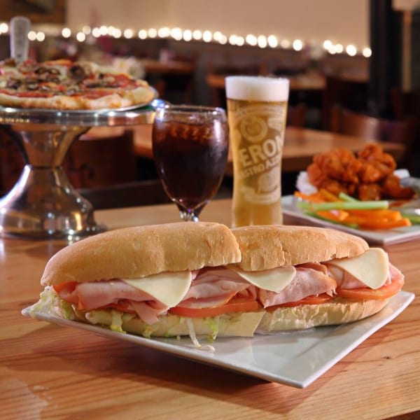 Mercato's Italian sub sandwich, pizza, wings, and drinks on a wooden table in a restaurant.