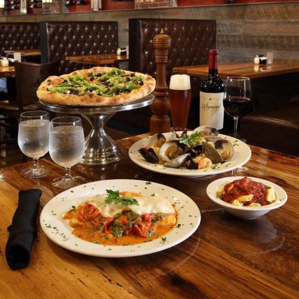 Mercato's Italian Grill table with pizza, pasta, clams, wine, and beer in a cozy restaurant setting.