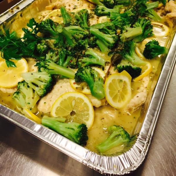 Italian chicken piccata with lemon slices, broccoli, and parsley in a foil pan.