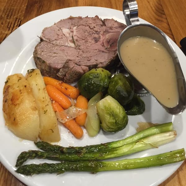 A Mercato's Italian grill plate with sliced meat, roasted potatoes, carrots, Brussels sprouts, asparagus, and gravy.