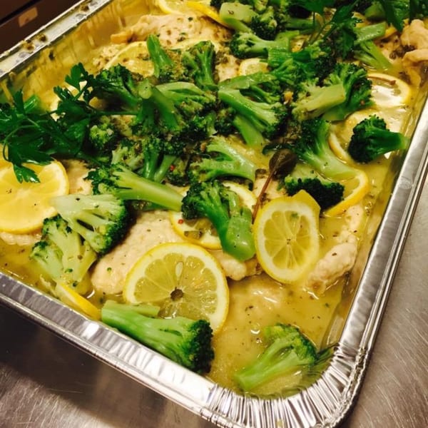 Italian chicken with broccoli, lemon slices, and capers in a foil pan.