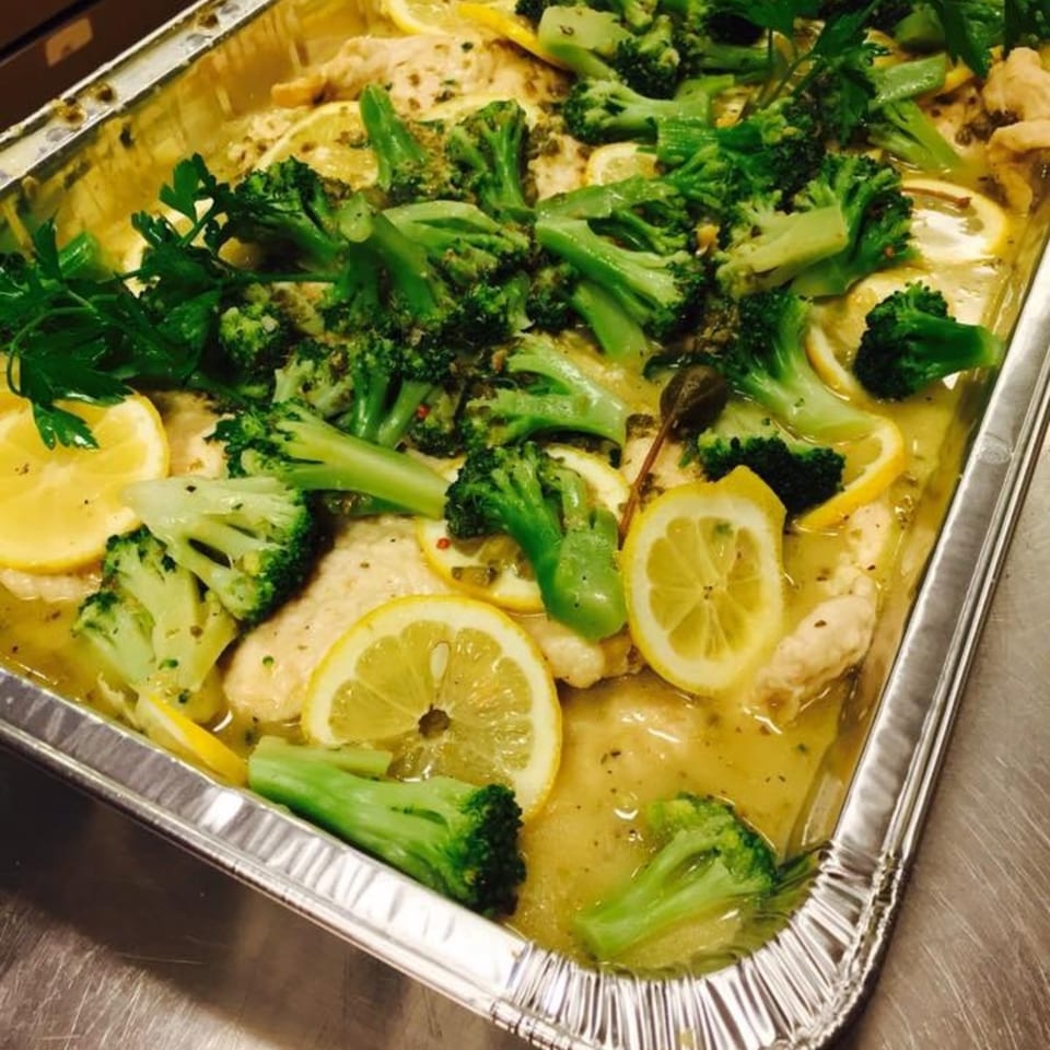 Italian chicken with broccoli, lemon slices, and capers in a foil pan.
